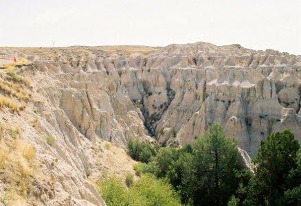 [Badlands pinnacles overlook into a basin with greenery.]